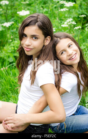 Portrait of two girls sitting back to back Stock Photo - Alamy