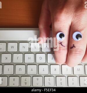 Google eyes and smiley face drawn on a hand, typing on keyboard Stock Photo
