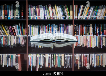 An open book on table front of shelves filled with books Stock Photo