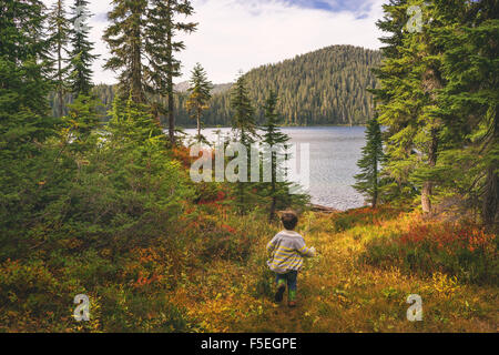 Boy running through forest towards lake Stock Photo
