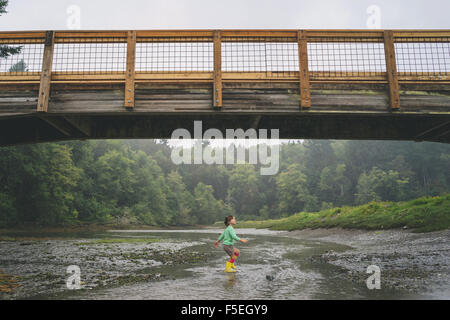 Girl playing in shallow water under bridge Stock Photo