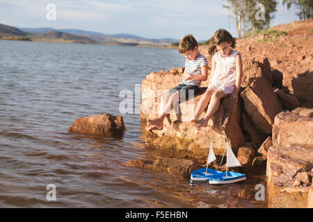 Boy and girl sitting on a rock by lake Stock Photo