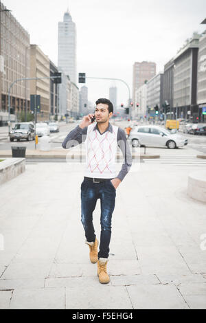 Young handsome indian contemporary business man walking through the city talking smartphone - technology, network, business, finance concepts Stock Photo