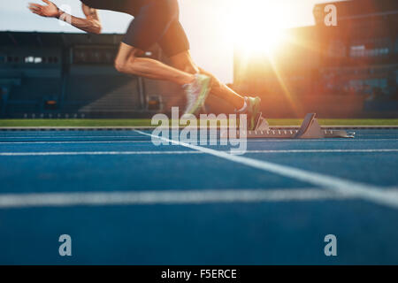 Athlete running on athletic racetrack. Low section shot of male runner starting the sprint from the starting line with bright su