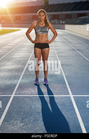 Full length portrait of young woman on stadium preparing herself for a run. Determined female athlete standing on the track with Stock Photo