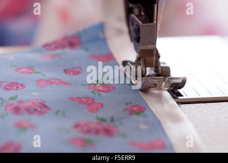 Concept image for sewing and making - close up of a sewing machine foot sewing binding onto a pretty blue and pink floral fabric Stock Photo