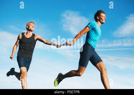 Portrait of young athletes pass the baton in a track relay against sky. Young runner practicing a relay race. Stock Photo