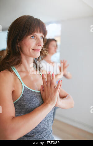 Women doing yoga exercises in class, standing in Tree Pose, Vrikshasana with namaste gesture looking way smiling. Stock Photo