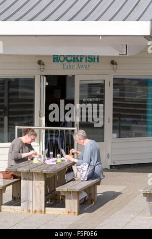 Two women eating fish and chips on the terrace of the Rockfish restaurant in Sutton Harbour, Plymouth, Devon, England Stock Photo