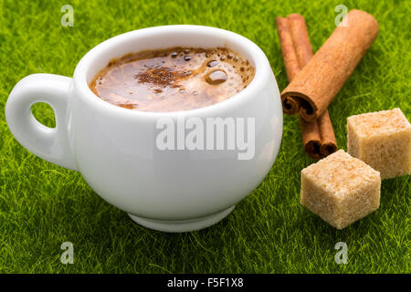Coffee hot cup and cinnamon sticks with cubes brown cane sugar on the green grass. Stock Photo