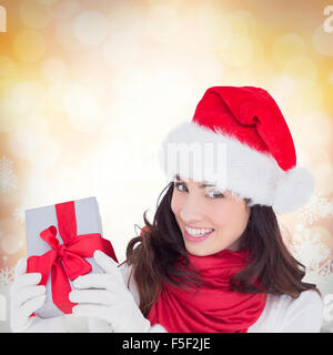 Composite image of excited brunette in santa hat showing gift Stock Photo