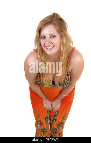 A lovely teenage girl with blond hair and a colorful orange long dress standing and bending down to the camera, over white Stock Photo