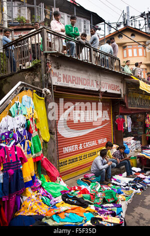 India, Himachal Pradesh, Shimla (Simla), Lower Bazaar, boys idling on balcony above clothes stall Stock Photo
