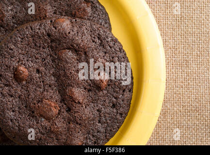 Top close view of freshly baked chocolate chip crispy brownie cookies on a yellow paper plate atop a burlap tablecloth Stock Photo