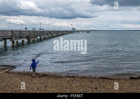 Small boy in blue hoodie top throwing pebbles into the sea Stock Photo