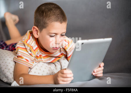 Little boy lying in bed and watch a story on touchscreen tablet Stock Photo