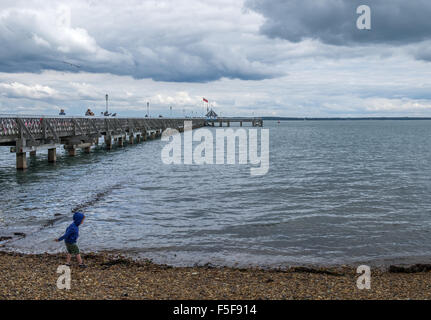 Small boy in blue hoodie top throwing pebbles into the sea Stock Photo