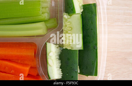 Top close view of snack vegetables with cucumbers celery and carrots in a plastic tray atop a wood table Stock Photo
