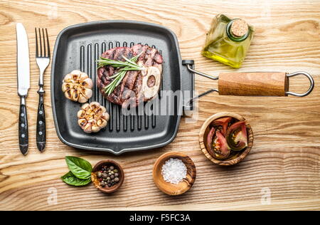 Beef steak with spices on pan on wooden table. Stock Photo