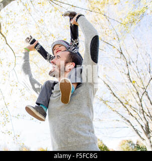 Portrait of happy father giving son piggyback ride on his shoulders in autumn park. Stock Photo