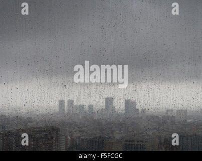 After heavy rainfall, the diffuse skyline of Barcelona is emerging in the twilight behind raindrops on a window. Stock Photo