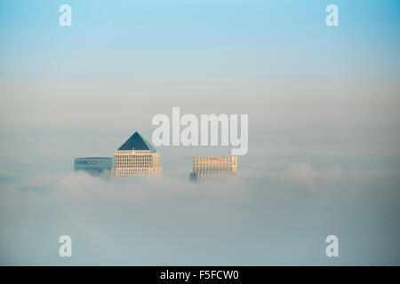 The roof tops of docklands high rise buildings protruding through the rising fog and clouds against a blue sky before sunset. Stock Photo