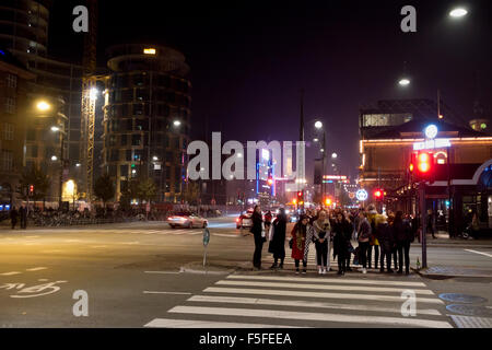 People crossing Bernstorffsgade in Copenhagen between Tivoli and Central Station a dark winter night. Left the new Axel Towers, Tivoli to the right Stock Photo