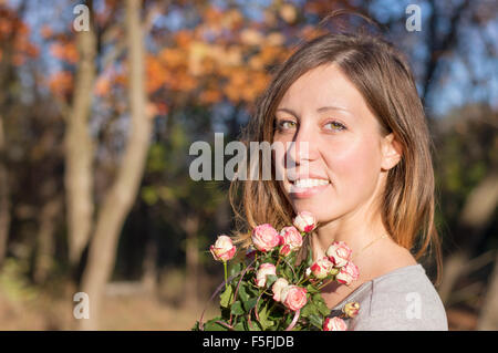 Portrait of a  happy brunette girl holding miniature roses in the forest on an autumn day Stock Photo