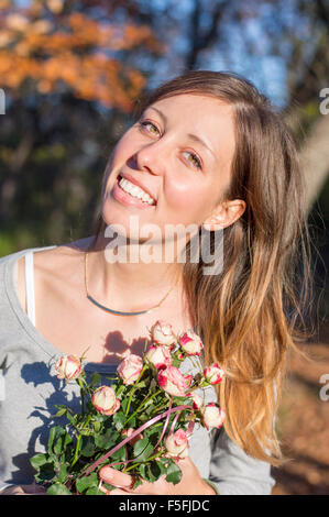 Happy brunette girl holding miniature roses in the forest on an autumn day Stock Photo