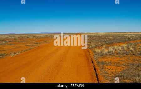 Long red dirt road in Australian outback stretching across arid treeless plains of  Flinders Ranges desert region to distant horizon & blue sky