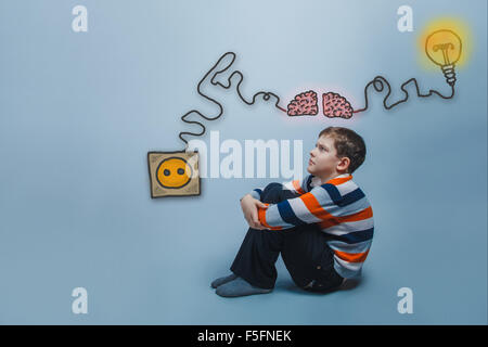 boy sitting on the floor hugging his arms legs and looking up ch Stock Photo