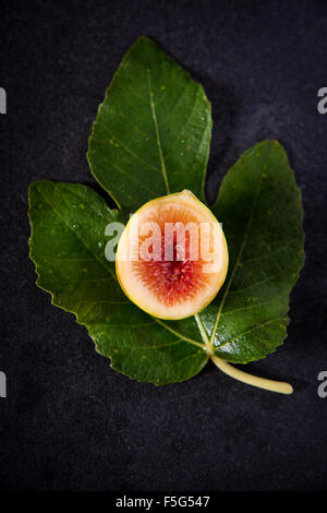 A fresh fig cut in half with a fig leaf on a dark background. These small Italian figs are very sweet and delicious! Stock Photo