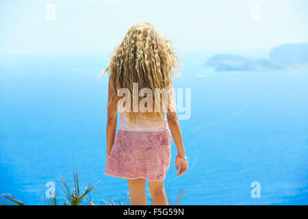 Blond girl looking blue Mediterranean sea as a tourist in Spain rear back view Stock Photo