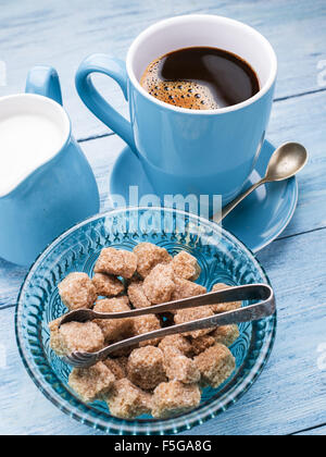 Cup of coffee, milk jug and cane sugar cubes on old wooden table. Stock Photo