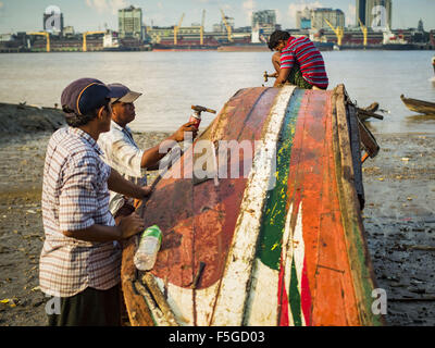 Nov. 4, 2015 - Dala, Yangon Division, Myanmar - Workers repair the hull of a small wooden ferry on the banks of the Yangon River in Dala, Yangon is in the background. Dala is located on the southern bank of Yangon River across from downtown Yangon, Myanmar. Many Burmese live in Dala and surrounding communities and go across the river into central Yangon for work. Before World War 2, the Irrawaddy Flotilla Company had its main shipyards in Dala. That tradition lives on in the small repair businesses the work on the hundreds of small wooden boats that serve as commuter ferries for the people of  Stock Photo