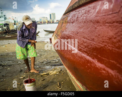 Nov. 4, 2015 - Dala, Yangon Division, Myanmar - A worker repaints a small wooden ferry on the banks of the Yangon River in Dala. Dala is located on the southern bank of Yangon River across from downtown Yangon, Myanmar. Many Burmese live in Dala and surrounding communities and go across the river into central Yangon for work. Before World War 2, the Irrawaddy Flotilla Company had its main shipyards in Dala. That tradition lives on in the small repair businesses the work on the hundreds of small wooden boats that serve as commuter ferries for the people of Yangon. The boats are pulled up onto t Stock Photo