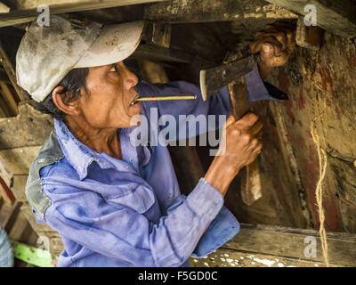 Nov. 4, 2015 - Dala, Yangon Division, Myanmar - A worker repairs the hull of a small wooden ferry on the banks of the Yangon River in Dala. Dala is located on the southern bank of Yangon River across from downtown Yangon, Myanmar. Many Burmese live in Dala and surrounding communities and go across the river into central Yangon for work. Before World War 2, the Irrawaddy Flotilla Company had its main shipyards in Dala. That tradition lives on in the small repair businesses the work on the hundreds of small wooden boats that serve as commuter ferries for the people of Yangon. The boats are pulle Stock Photo