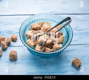 Cane sugar cubes in the old-fashioned glass plate on wooden table. Stock Photo