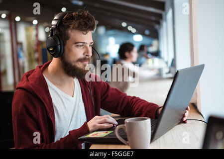 Concentrated handsome male with beard using headset and laptop Stock Photo