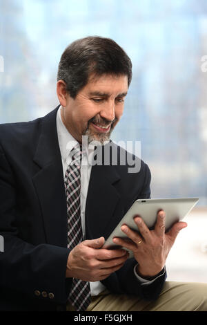 Portrait of Hispanic businessman using electronic tablet near office window Stock Photo