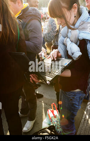 Student using a laptop computer in a crowd of people, in Trafalgar Square, London, England, UK. Stock Photo