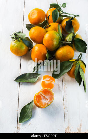 A bunch of juicy tangerines with green leaves on a white wooden background Stock Photo