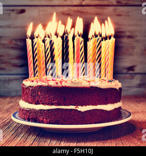 a cake topped with some lit candles before blowing out the cake, on a rustic wooden table, with a filtered effect Stock Photo