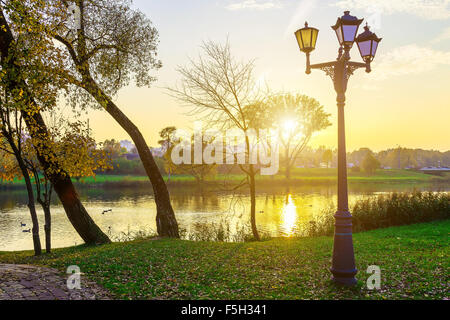 Landscape in Park with Trees and Lamps near Lake at Sunset in Autumn Stock Photo