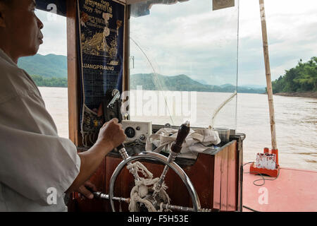 A river boat captain steers a tourist boat along the Mekong river near Luang Prabang in Laos Stock Photo