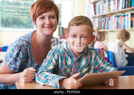 School Pupil With Teacher Using Digital Tablet In Classroom Stock Photo