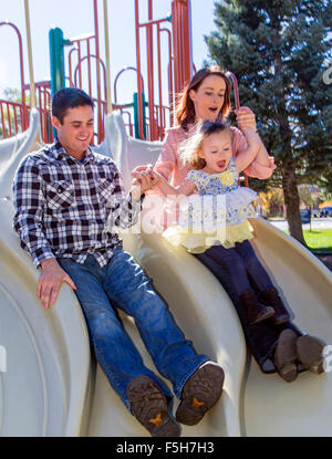 Father, mother and cute young daughter playing on park sliding board Stock Photo