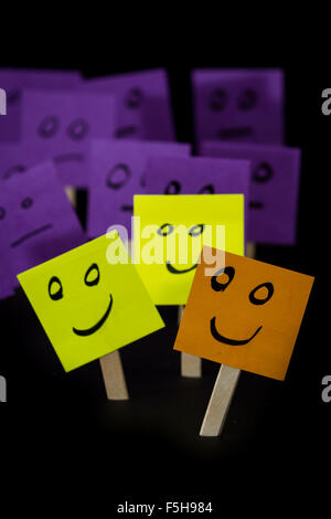 conceptual image using sticky notes with hand drawn faces on them isolated on a black background Stock Photo