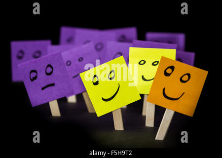 conceptual image using sticky notes with hand drawn faces on them isolated on a black background Stock Photo