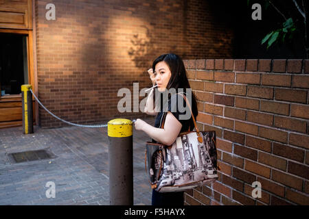 New York City, New York, USA.  August 23, 2015:  A woman stops to adjust her hair with an unlit cigarette in her mouth. Stock Photo